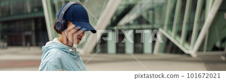 Sportive woman in headphones stands with bottle of water after running in city. Healthy lifestyle Sportive woman in headphones stands with bottle of water after running in city. Healthy lifestyle 101672021