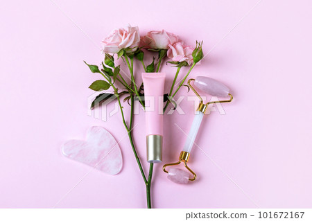 Pink jade roller and gua sha for face massage with cream or gel for the face and flower roses. Facial massager tools. Anti age, lifting and toning care. Modern selfcare concept. Pink jade roller and gua sha for face massage with cream or gel for the face and flower roses. Facial massager tools. Anti age, lifting and toning care. Modern selfcare concept. 101672167