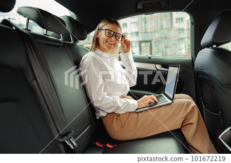Attractive businesswoman in glasses working on laptop sitting car backseat and looking at camera 101672219