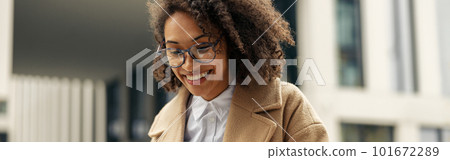 Happy african business woman working laptop while sitting outside on background of office building 101672289