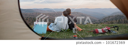 View from inside tent on couple in love hugging and resting on peak of mountain. Beautiful nature. View from inside tent on couple in love hugging and resting on peak of mountain. Beautiful nature. 101672369