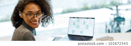 Smiling woman freelancer working laptop and making notes while sitting near windows in cozy cafe 101672543