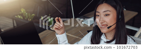 Young woman using headset and computer while talking with customers online Young woman using headset and computer while talking with customers online 101672703