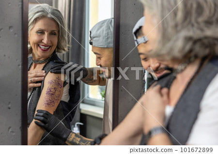 Long-haired woman looking in the mirror at her new tattoo Long-haired woman looking in the mirror at her new tattoo 101672899