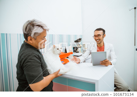 a male vet bring a tablet while meeting a cat and it's owner a male vet bring a tablet while meeting a cat and it's owner 101673134