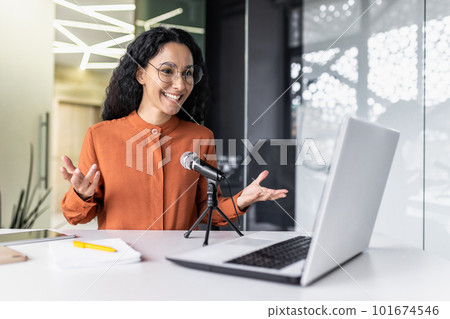 Successful Latin American businesswoman blogger recording online video podcast inside modern office, female worker using professional microphone for online stream and laptop, smiling and gesturing. Successful Latin American businesswoman blogger recording online video podcast inside modern office, female worker using professional microphone for online stream and laptop, smiling and gesturing. 101674546