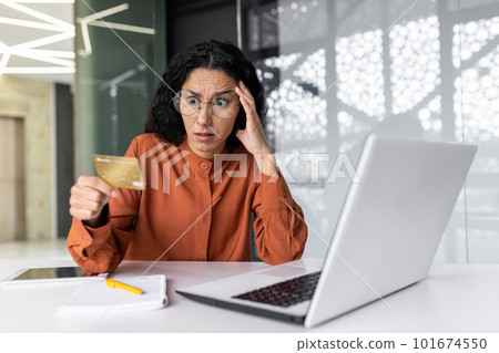 Dissatisfied and angry businesswoman inside the office, hispanic woman at workplace cheated by online fraudsters, female employee trying to transfer money from bank credit card, received error. Dissatisfied and angry businesswoman inside the office, hispanic woman at workplace cheated by online fraudsters, female employee trying to transfer money from bank credit card, received error. 101674550