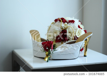 A pair of white women's high heels and a beautiful rose flower bucket. 101674885