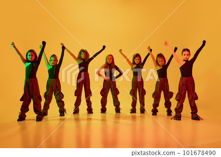Group of talented children, little girls in sportive casual style clothes dancing hip-hop, contemporary dance against yellow studio background in neon light Group of talented children, little girls in sportive casual style clothes dancing hip-hop, contemporary dance against yellow studio background in neon light 101678490