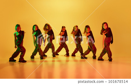 Little artistic girls, children in sport style clothes dancing hip-hop against yellow studio background in neon light. Beauty of movements 101678514