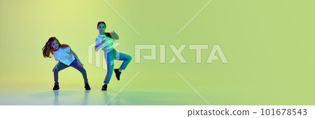 Active, talented little girls, children in casual clothes dancing against green studio background in neon light Active, talented little girls, children in casual clothes dancing against green studio background in neon light 101678543