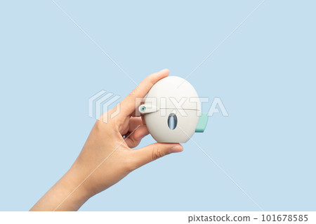 Asthma and COPD concept. Female hand holding Tiotropium bromide inhaler on blue background. Pharmaceutical device of bronchodilator for lung inflammation treatment and prevent asthma attack. Asthma and COPD concept. Female hand holding Tiotropium bromide inhaler on blue background. Pharmaceutical device of bronchodilator for lung inflammation treatment and prevent asthma attack. 101678585