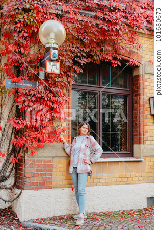 a beautiful girl stands against the background of the window of an old European house, entwined with a floating red color in autumn. Tourism & Travel Concept. Nice portrait of a young woman, in boho 101680673