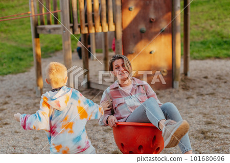 Mother and son having fun on a swing. Motherhood and childhood concept. Sunny summer day. Beautiful family is having fun outside. Parents with children riding on a swing. Mom is playing with her 101680696