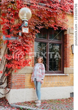 a beautiful girl stands against the background of the window of an old European house, entwined with a floating red color in autumn. Tourism & Travel Concept. Nice portrait of a young woman, in boho 101680798