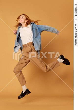 One young red haired pretty girl, student wearing casual clothes jumping with joy at camera over ginger background. Happiness, joyful 101680801
