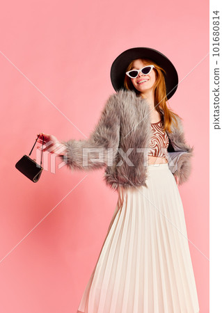 Portrait of one stunning girl wearing stylish look with fur jacket, black hat and mini handbag over pink background. Young fashionista Portrait of one stunning girl wearing stylish look with fur jacket, black hat and mini handbag over pink background. Young fashionista 101680814