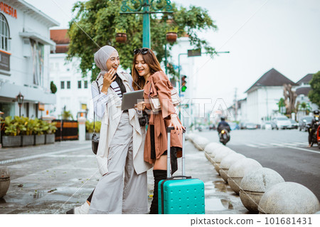 two female travellers laughing while standing together at the sidewalk 101681431