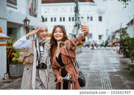 two female travellers taking selfie photo using the phone 101681497