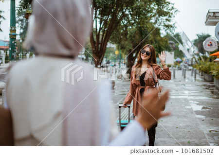 female traveller with glasses waving her hand to her friend 101681502