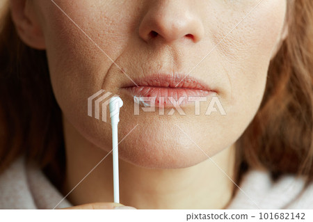 Woman applying ointment using cotton swab against beige Woman applying ointment using cotton swab against beige 101682142