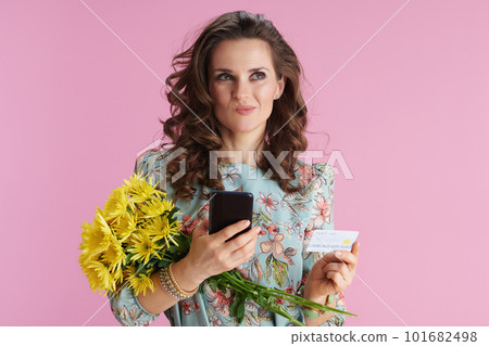 doubting woman in floral dress using phone applications on pink 101682498