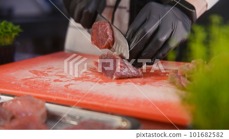 Professional cook in apron cuts pieces of meat on slices Professional cook in apron cuts pieces of meat on slices 101682582