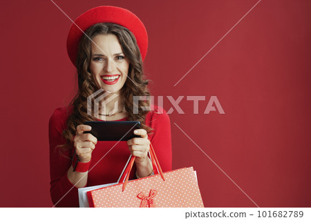 happy woman in dress and beret with shopping bags using phone 101682789