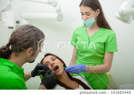Woman sitting in dental chair at medical center while professional doctor fixing her teeth 101683449