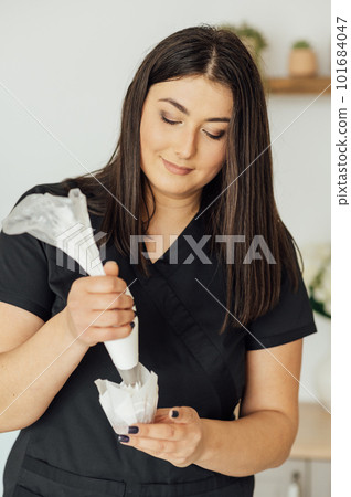 The girl cook puts the cream from the mixer into the mold for decorating cakes The girl cook puts the cream from the mixer into the mold for decorating cakes 101684047