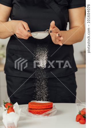 The cook sprinkles flour on a red cake through a sieve The cook sprinkles flour on a red cake through a sieve 101684076