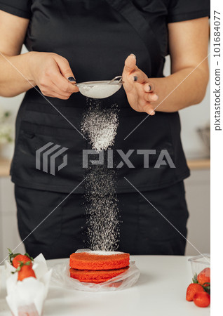 The cook sprinkles flour on a red cake through a sieve 101684077