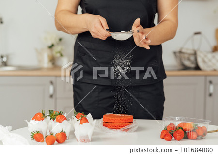 The cook sprinkles flour on a red cake through a sieve 101684080