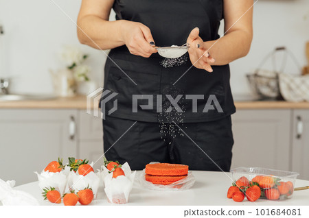 The cook sprinkles flour on a red cake through a sieve The cook sprinkles flour on a red cake through a sieve 101684081