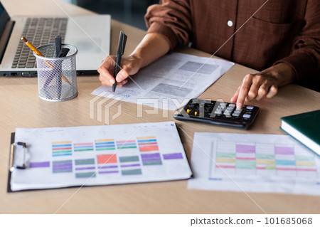 Close-up photo. Female hands of an accountant, auditor, financier, banker working in the office at a table with documents and with a laptop, using a calculator. 101685068