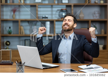Successful businessman in home office celebrating victory and success, mature adult male boss satisfied with achievement results holding hands up triumph gesture financier happy using laptop at work Successful businessman in home office celebrating victory and success, mature adult male boss satisfied with achievement results holding hands up triumph gesture financier happy using laptop at work 101685082