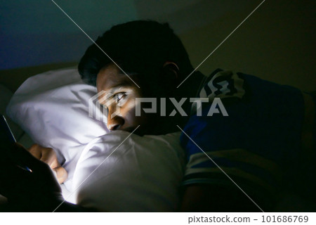 young man sitting on bed using smart phone at night young man sitting on bed using smart phone at night 101686769
