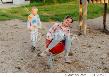 Mother and son having fun on a swing. Motherhood and childhood concept. Sunny summer day. Beautiful family is having fun outside. Parents with children riding on a swing. Mom is playing with her 101687566