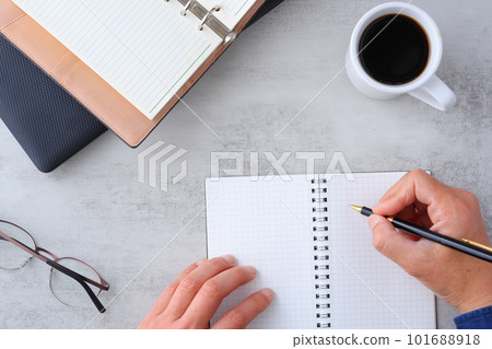 Image of both hands of a man who spreads a laptop and notebook on the desk and does desk work while drinking coffee Image of both hands of a man who spreads a laptop and notebook on the desk and does desk work while drinking coffee 101688918