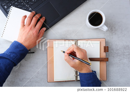 Image of both hands of a man who spreads a laptop and notebook on the desk and does desk work while drinking coffee 101688922