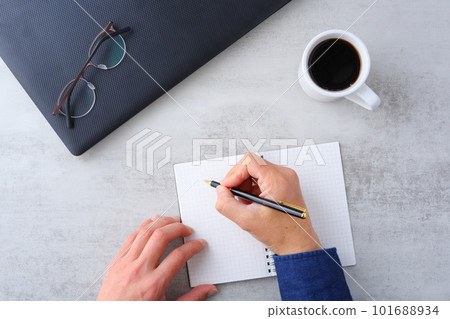 Image of both hands of a man who spreads a laptop and notebook on the desk and does desk work while drinking coffee Image of both hands of a man who spreads a laptop and notebook on the desk and does desk work while drinking coffee 101688934