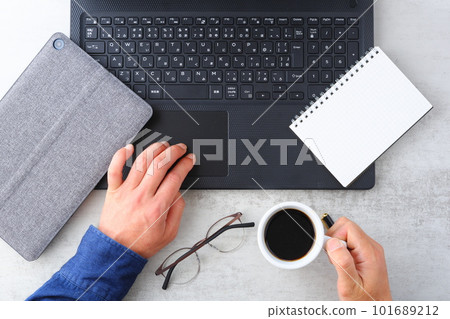 Image of both hands of a man working at a desk with a laptop while drinking coffee 101689212