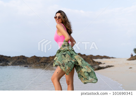 Stylish romantic tender athletic slim sensual woman in pink swimsuit, tropical kimono and sunglasses on the beach at sunset 101690341