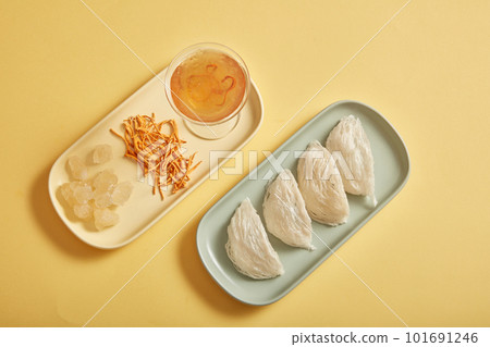 Top view of raw bird nest, cordyceps and rock sugar. A bottle of unlabeled bird nest water and glass cup of bird nest soup on yellow background Top view of raw bird nest, cordyceps and rock sugar. A bottle of unlabeled bird nest water and glass cup of bird nest soup on yellow background 101691246
