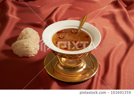 The food warmer filled with bird nest soup with jujube and dried goji berries, decorated with edible bird nest on a pink fabric background. Benefiting people health, skin and bone The food warmer filled with bird nest soup with jujube and dried goji berries, decorated with edible bird nest on a pink fabric background. Benefiting people health, skin and bone 101691359