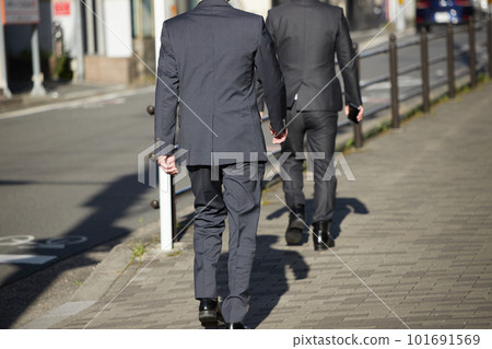 Rear view of two businessmen walking on a sidewalk in the city at daytime 101691569