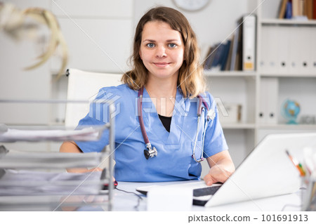 Positive woman doctor sitting at workplace with computer in office 101691913
