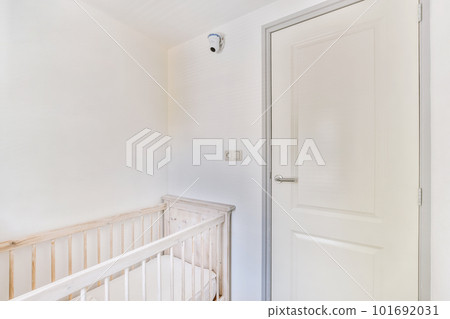 Interior of white room with baby crib and armchair near window with blue chest of drawers in daylight 101692031