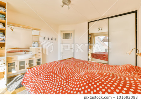 a bedroom with red and white polka dot bedspreed in the middle of the room, there is a mirror on the wall 101692088