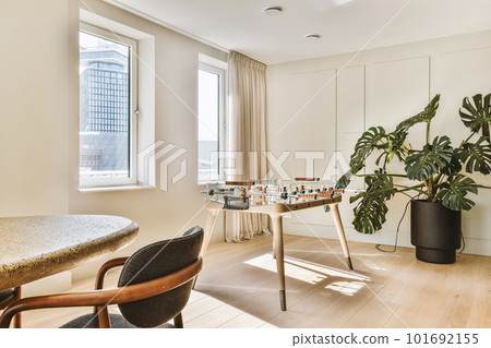 Contemporary minimalist style interior design of light studio apartment with wooden table and chairs in dining zone between open kitchen and living room with white walls and parquet floor Contemporary minimalist style interior design of light studio apartment with wooden table and chairs in dining zone between open kitchen and living room with white walls and parquet floor 101692155